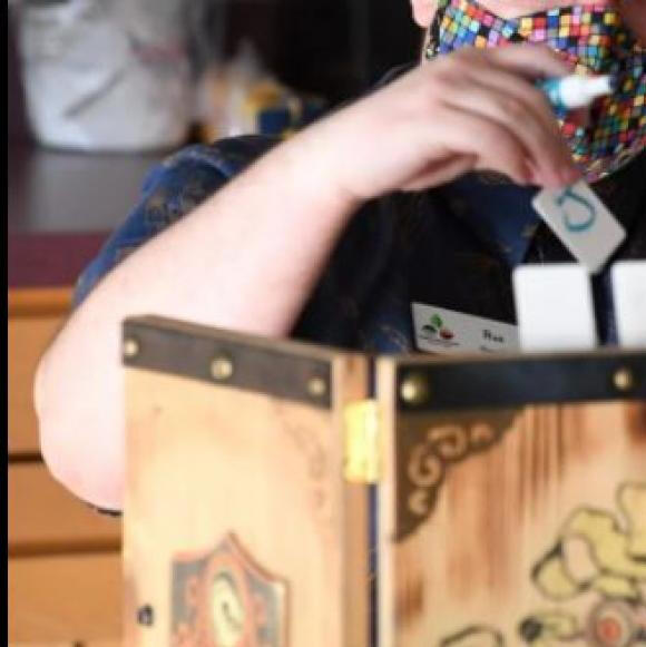 An image of Rue wearing a mask and sitting behind a DM screen